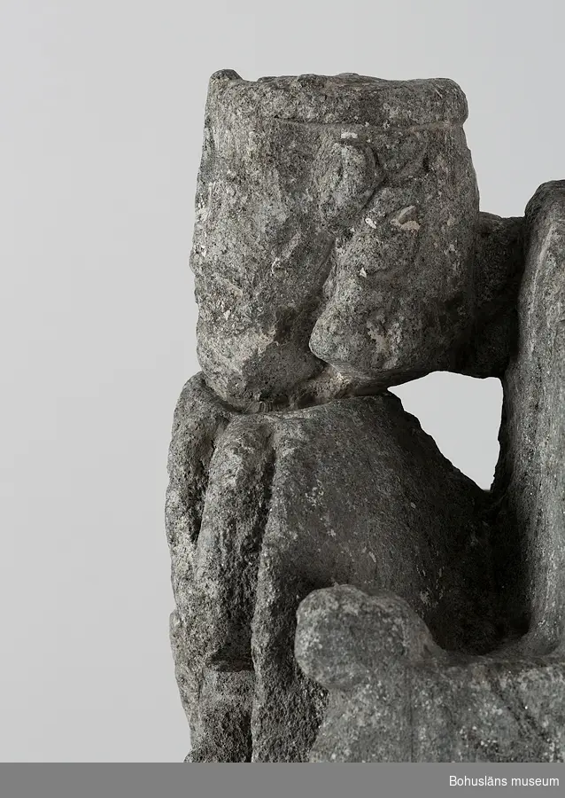 Stenskulptur av täljsten från Svarteborgs kyrka. Den helige Olof sittande i tronstol med högt ryggstöd. Han bär livbälte och mantel, en murkrona på huvudet, möjligen ett relikvarium i höger hand och håller vänster hand om skägget. Skulpturen är starkt eroderad.

Ur handskrivna katalogen 1957-1958: Olav d. helige, täljsten, Svarteborg. M: H. 41, största Br. 32,5 cm; krona och mantel, i höger hand spiran, vänster griper om skägget; sittande på en tronstol m. armstöd och högt ryggstöd, på alla håll smalnar stolen av uppåt. Starkt sliten.

Ur Katalog 1. Uddevalla Museihistoriska samlingar, svenska avdelningen. A. Yngre föremål. Upprättad av Knut Adrian Andersson 1916:                                                                                                                              No 34. Bild i täljsten av Olov den Helige. Yngre medeltiden, räknad till 1550. Förvarats i Svarteborgs kyrka under namnet "Kung Rane". Skänkt av församlingen år 1860-70-tal till Uddevalla museum. Förvaras ovanpå Medeltidsskåpet i sydvästra rummet.

Presenterad i  Uddevalla Museums tryckta katalog 1869 under rubriken 
F] Saker från yngre Medeltiden, räknad till 1550.
N:o 1. Bilder af S:t Olof i sten från Svarteborgs kyrka.

1861-1870 1 Arkeologiska och Etnografiska samlingarna U-a Museum D4A 1
Ur Gåvobok1864:
Svarteborgs församling:
Kristusbild af träd samt fragmenter af en Granit- [överstruket] Täljstensbild, enligt sägen föreställande Kung Rane, hvilka begge setat [överstruket] [oläsligt tillägg] i Svarteborgs kyrka. 
Tillagd kommentar av inrendent Knut Adrian Andersson; Olof d. Helige troligen.

Se foton på föremålet i Uddevalla museums kyrkliga utställning 1920, UMFA54467:0089.
Tillstånd, se Vårdblankett.