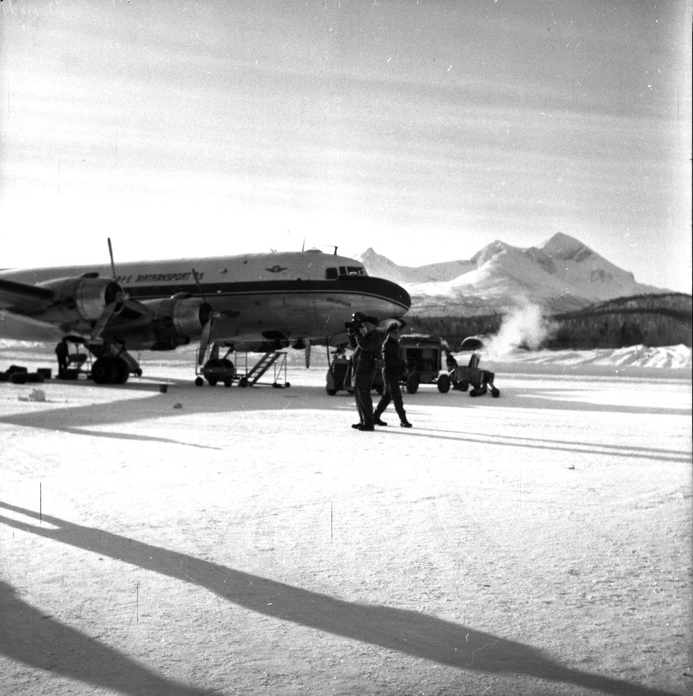 Lufthavn/Flyplass. Bardufoss. Et fly, LN-SUP, Douglas C-54B, Skymaster fra Braathens SAFE, parkert mellom snøfonnene på oppstillingsplassen (tarmac).