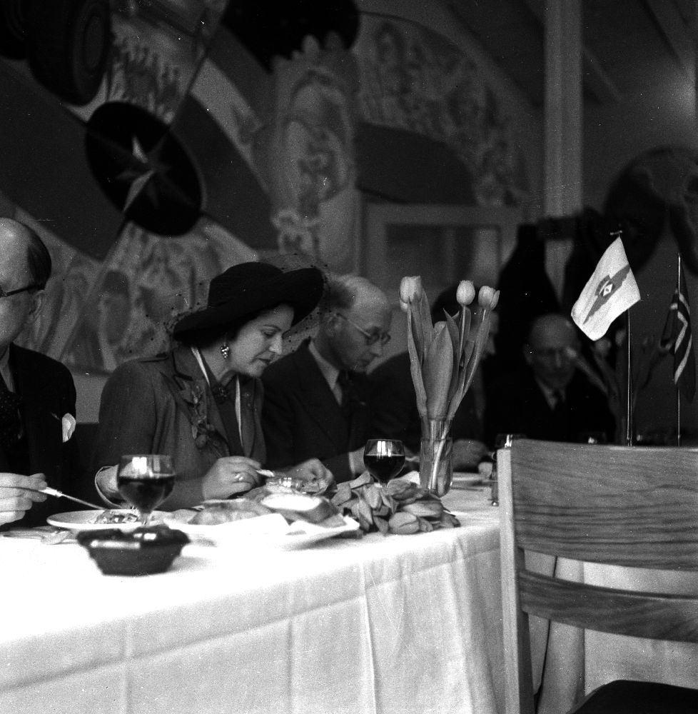 Landskap. Amsterdam. To personer inntar middag ved et spisebord. Braathens vimpel på bordet. De Braathens SAFE gjennomførte prøveflyvningen før oppstart ruteflyvning til Østen, foretok de flere mellomlandinger underveis.