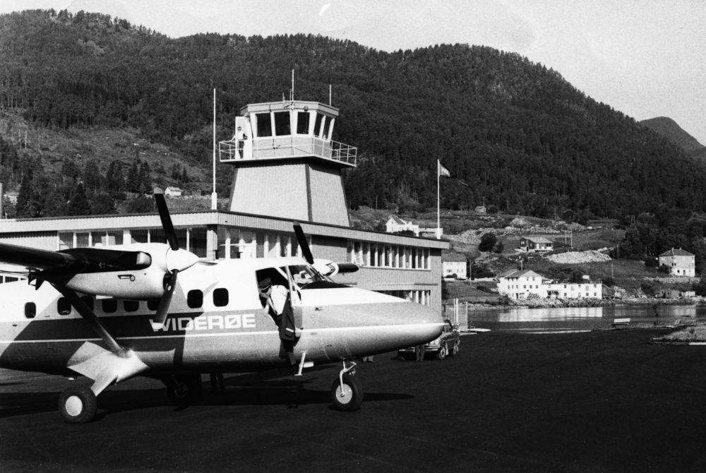 Lufthavn/Flyplass. Førde. Utenfor Flytårnet og ekspedisjonsbygget står et fly, DHC-6 Twin Otter fra Widerøe parkert. En flyger/pilot på vei ut av cockpit.