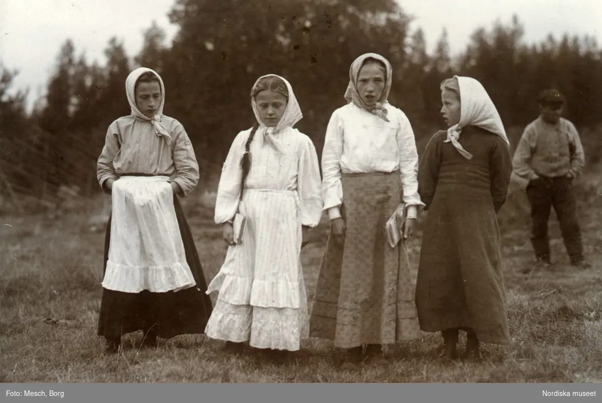 Läsflickor från Teurajärvi, Korpilombolo, 1913. Fyra konfirmander i ljusa huvudkläden står på rad. I bakgrunden ses en man.