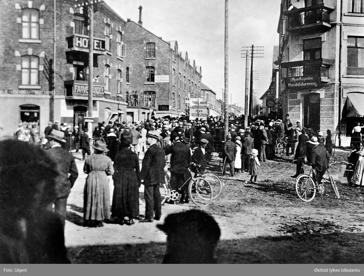 "Ned med kapitalismen - leve socialismen" - parole i 1. mai-demonstrasjon i Storgaten, Mysen, Eidsberg i 1921. Ved jernbanestasjonen. Ellers reklameskilt for Mysen Kooperative Handelsforening, Hotel & Farvehandel.