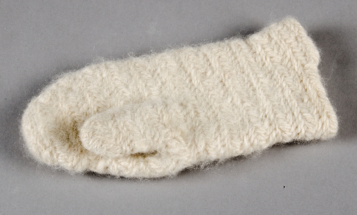 En tumvante i barnstorlek tillverkad i nålbindningsteknik av vitt ullgarn.