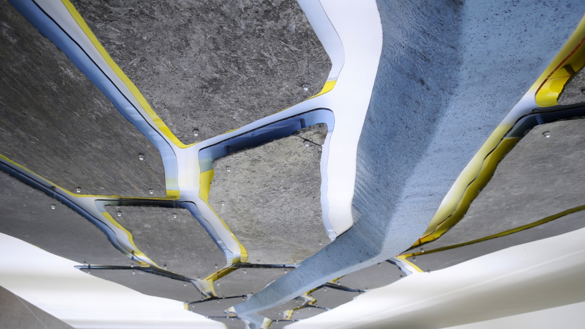 Vegginstallasjonen går over 3 etasjer og består av en hel hovedform som er støpt i glassfiber. Denne formen "tegner" bevegelsen i verket. Langs hele formen, på begge sider, er det montert skiferformer med en synlig "kontur" av farget plexiglass i gult og blått.