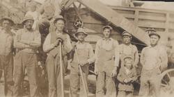 Gruppebilde av arbeidere foran treskeverk (?).