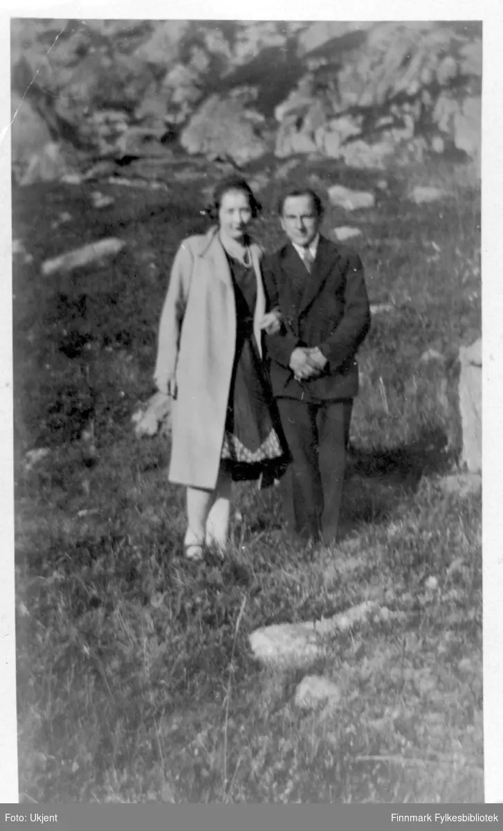 Dette bildet er av Vilmar Dahl og en ukjent kvinne. Vilmar muligens fra Øksfjord, Loppa kommune. Kvinnen er kledd i en lang frakk, et hodeplagg, kjole og har på seg et smykke. Vilmar er kledd i jakke, bukse og slips. I bakgrunnen kan man se stein.