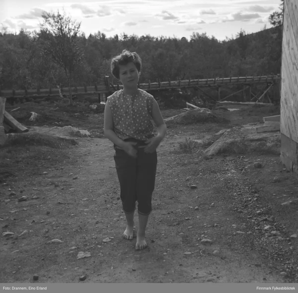 Turid Karikoski fotografert på en gårdsplass. Pga. vannrennen i bakgrunnen som er med på flere bilder i Drannem-samlingen, kan stedet være Luolajärvi i Finland.
