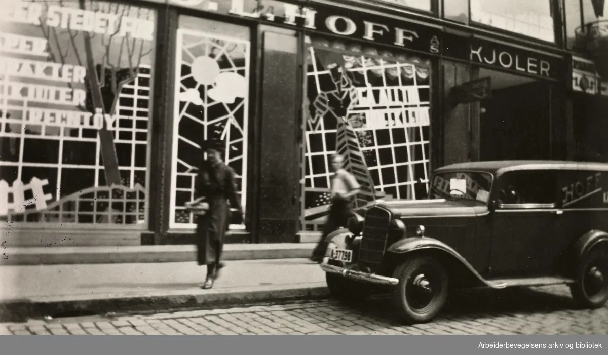 Ole M. Engelsens fotografier fra okkupasjonsårene i Oslo. Slik ble vindusrutene sikret for å hindre at glasset skulle splintres ved flyangrep. Lemmene og sanden skulle gjøre tilfluktsrommene i kjelleren tryggere..Bildet er tatt utenfor Hoff damekonfeksjon i Karls Johans gate 25, mai 1940.