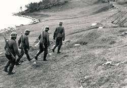 Soldater som går på en åker langs sjøen.