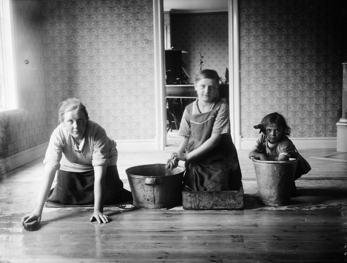 Sannolikt Helga och Helmy Melberg som skurar golv tillsammans med sin mor Frida Melberg, Revelsta gård, Altuna socken, Uppland 1918