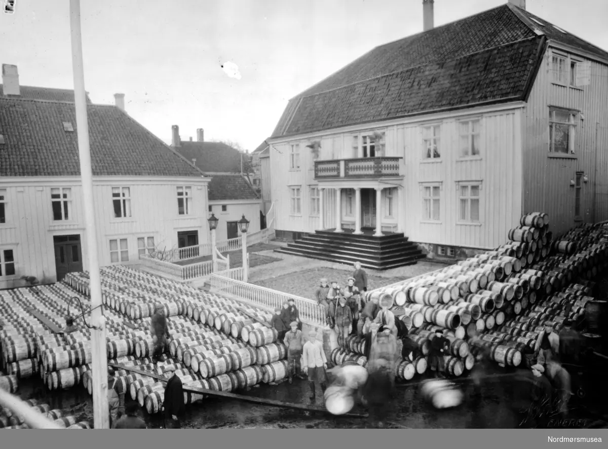Fra en kjøpmannsgård i Kristiansund, Parelius på Nordlandet hvor vi ser store deler av uteområdet rundt huset er fullt av sildtønner. Trolig fra samme serie som KMb-1944-000.0628 og fortløpende. Fra Nordmøre Museums fotosamlinger.