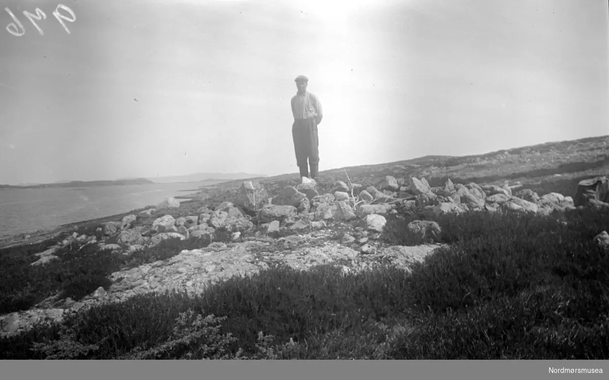 På bildet ser vi en gravrøys nord for Edøyvalens havbukt, nær Kulisvaet på Edøy. Se Yderstads notater, bind 7 side 346, nr. 9. Bildet er datert Juni 1948, og mest sannlig den 16. denne måneden. Personen på bildet er ukjent. Fra Nordmøre Museums fotosamlinger. 