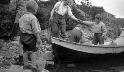 Tre gutter på vei ut av en robåt. En mann hjelper dem i land