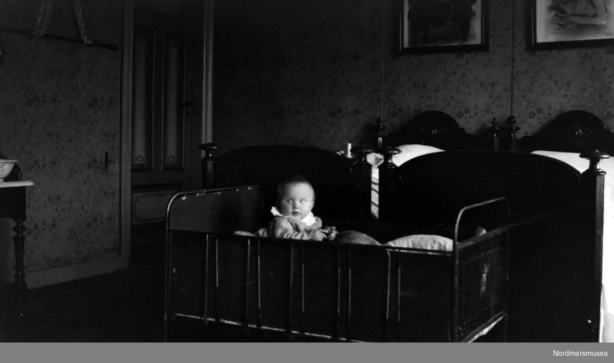 Trolig interiør fra Margrethe og Georg Sverdrups soverom, Barneseng med ett av deres barn i, bak foreldresengen. (Fra Nordmøre Museums fotosamlinger)
