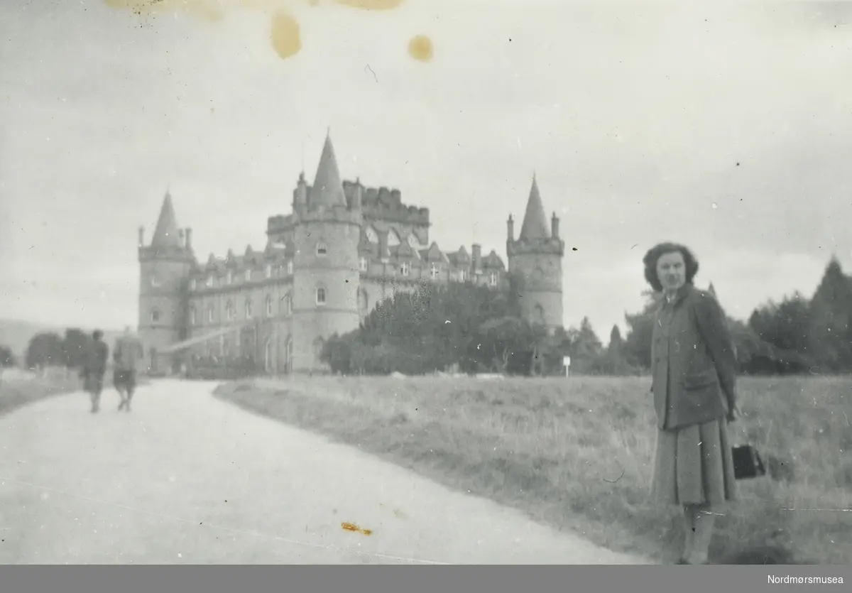 Foto av en kvinne stående ved en vei som leder opp til et stort slott i bakgrunnen. Muligens fra Tyskland. Det er litt usikkert hvem vi ser på bildet. Fra Nordmøre museums fotosamlinger.
