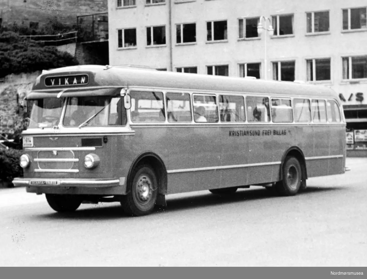 Bussen er registrert T-6114 og var en Scania-Vabis B71 personbuss med 30 sitteplasser og mange ståplasser. Karosseriet ble levert av Vestfold Bil og Karosseri (VBK). Bussen er 1958-modell registrert 16. desember. Bussen var i bruk til 1970. Kristiansund Frei Billag som hadde bussen i trafikk i dette tidsrommet. Fotografering er derfor tidligst fra desember 1958. (Info: Sveinung Berild - 15.10.2016). en av de lokale rutebussene i Kristiansund. Foran handelshuset Jonas Eriksen AS på Rådhusplassen.  Fra Nordmøre museums fotosamlinger.