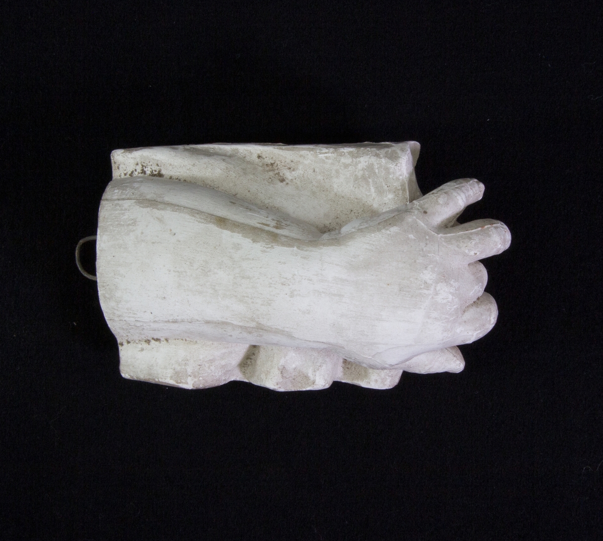 Studie av gips föreställande en hand och delar av armen som vilar på ett svängt underlag. Ögla för upphängning.
