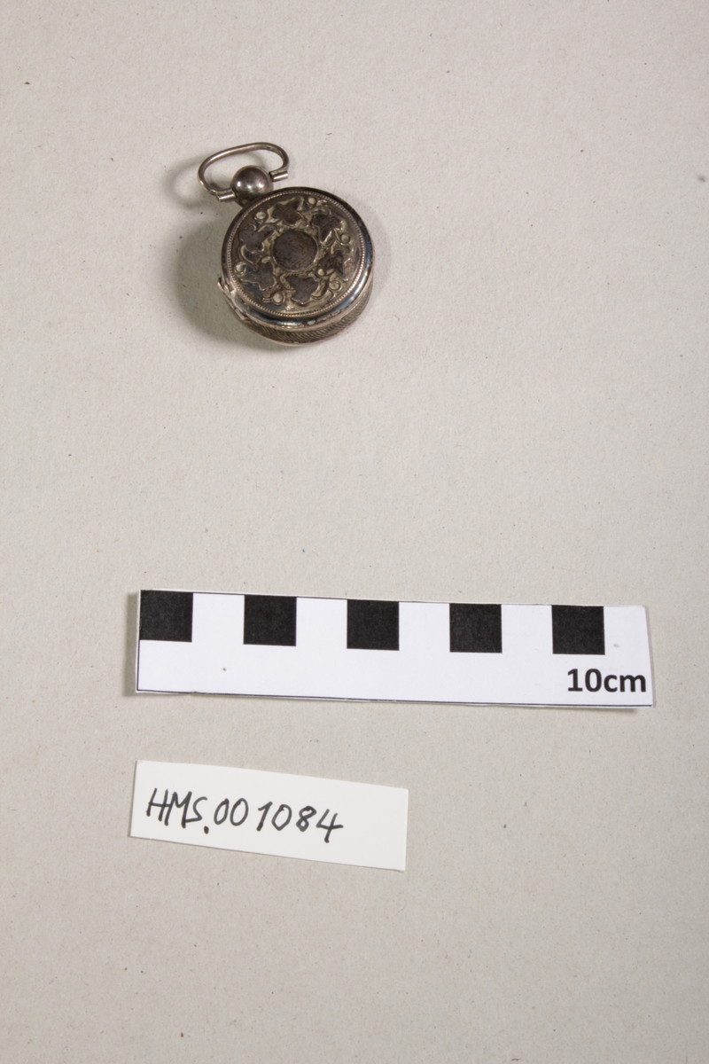 Sølv (?), i form av medaljong støpt vinbladdekor, på for- og bakside, indre lokk med gjennombrutt rankedekor, kule med bærering, forgylt innside. Diam. 4,7cm.