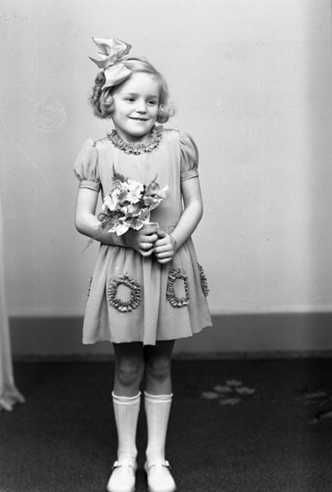 Foto av en okänd brudnäbb (flicka), i klänning med puffärm och stor rosett i håret.
Helfigur. Ateljéfoto.