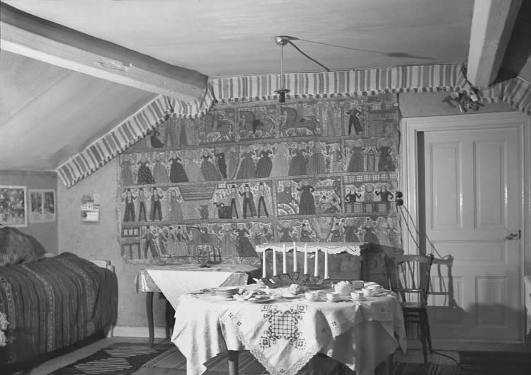 Interiör med ett julbord och till vänster syns en soffa. På väggen hänger 
en stor bonad med olika bilder.
