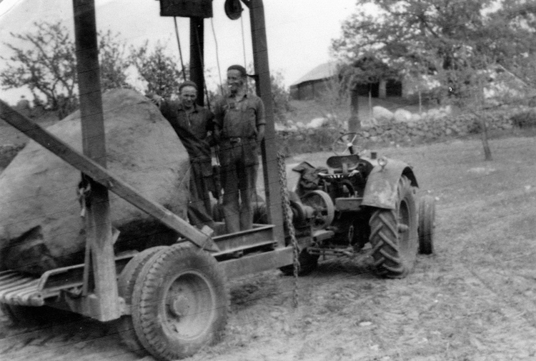 Foto av två män som står på en åker bredvid en stenvagn, förspänd med
en traktor.