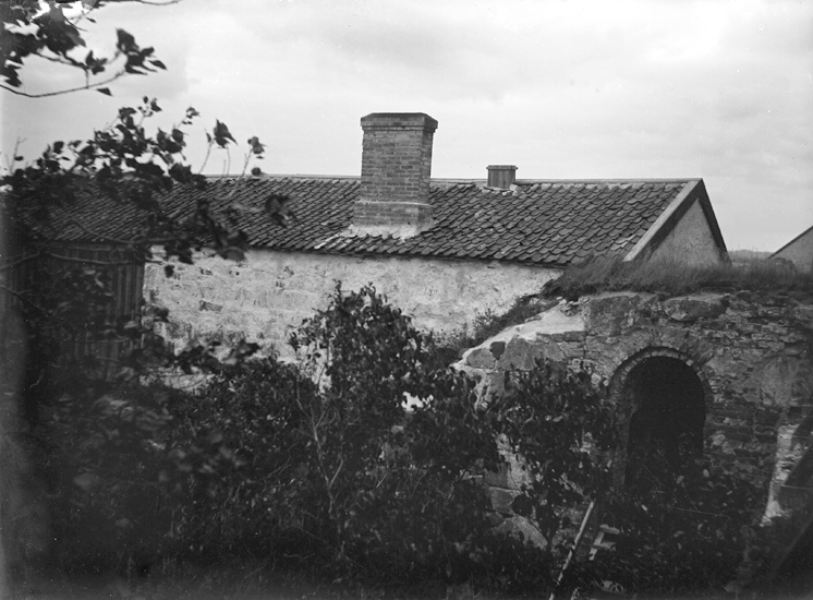 Foto av en magasinsliknande stenbyggnad. Till höger syns en port i muren.