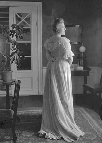 Kvinna med lång klänning i ett vardagsrum med glasdörr.