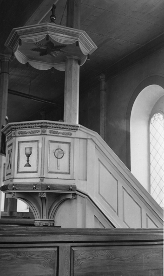 Foto på en predikstol med kyrkbänkar framför.