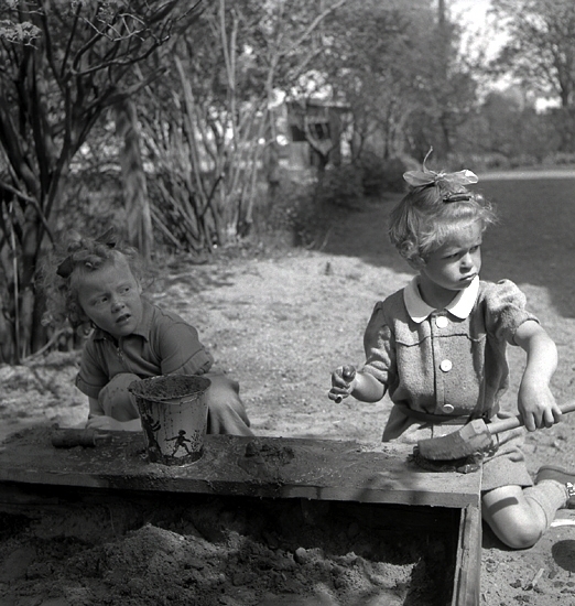 A-K Bergstrands kindergarten, 1942. 
Två flickor i en trädgård bakar "sandkakor."