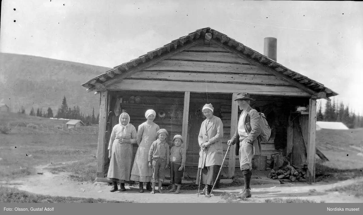 Gruppfoto framför en liten stuga, från början av 1900-talet.