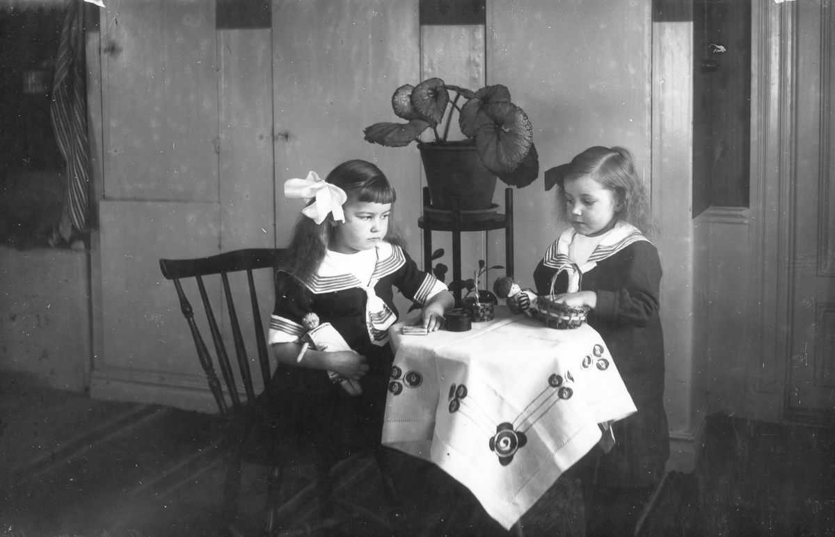 Interiör med  två flickor med leksaker som sitter vid ett litet bord.