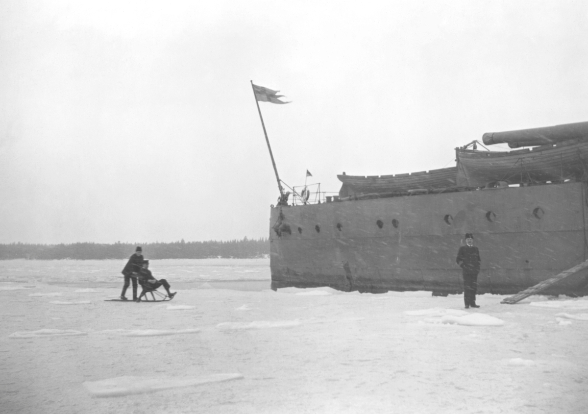 Svenska militärer åker sparkstötting på isen nedanför aktern på pansarskeppet SVERIGE under Ålandsexpeditionen 1918