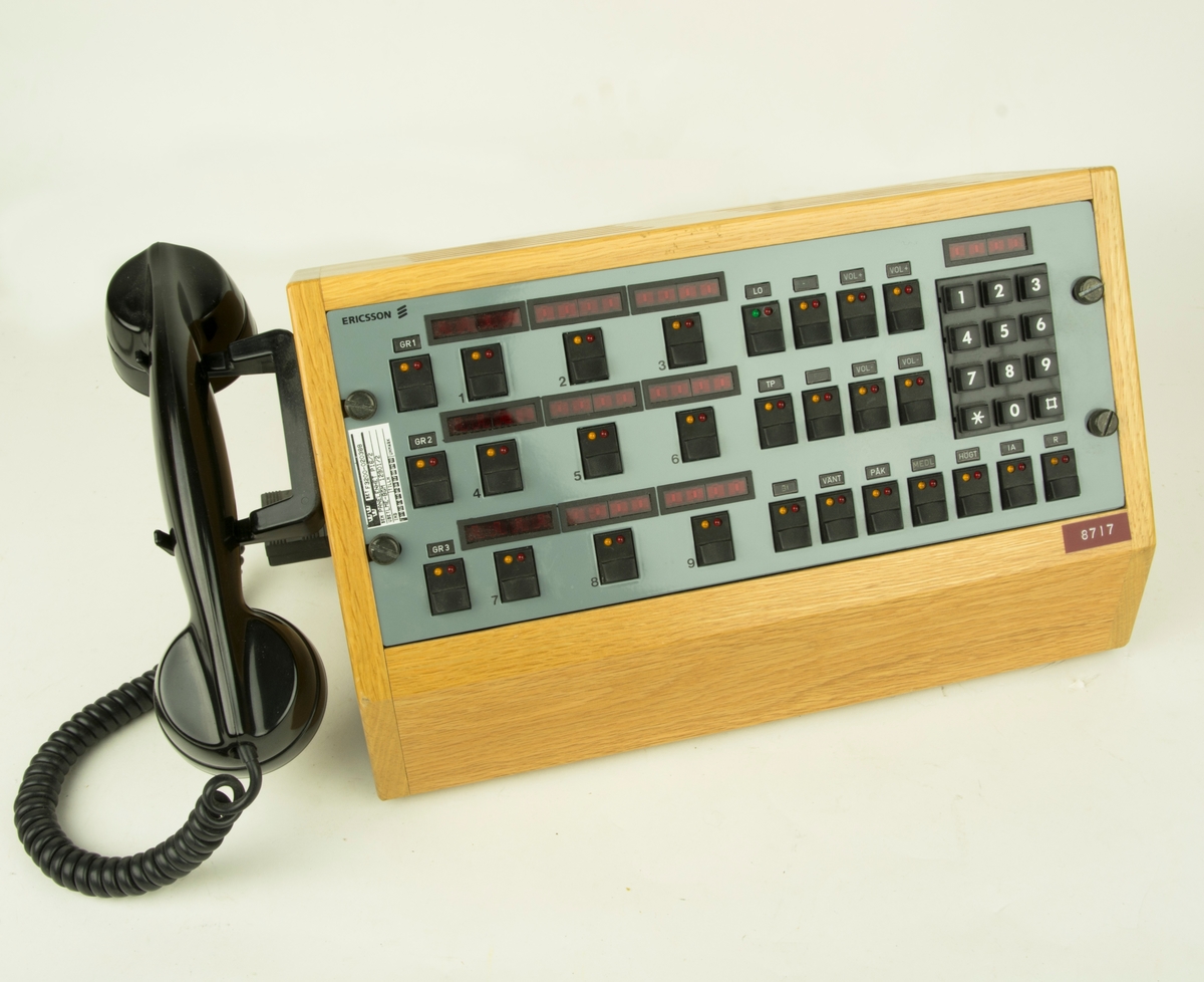 Panelenhet P16/2, telefonväxel. Telefonen består av en lur i svart plast kopplad till en träinfattad metallpanel med nummersats.