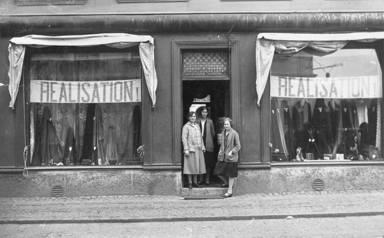 Manufakturaffär med tre biträden, i skyltfönstren hänger banderoller med texten "Realisation!"