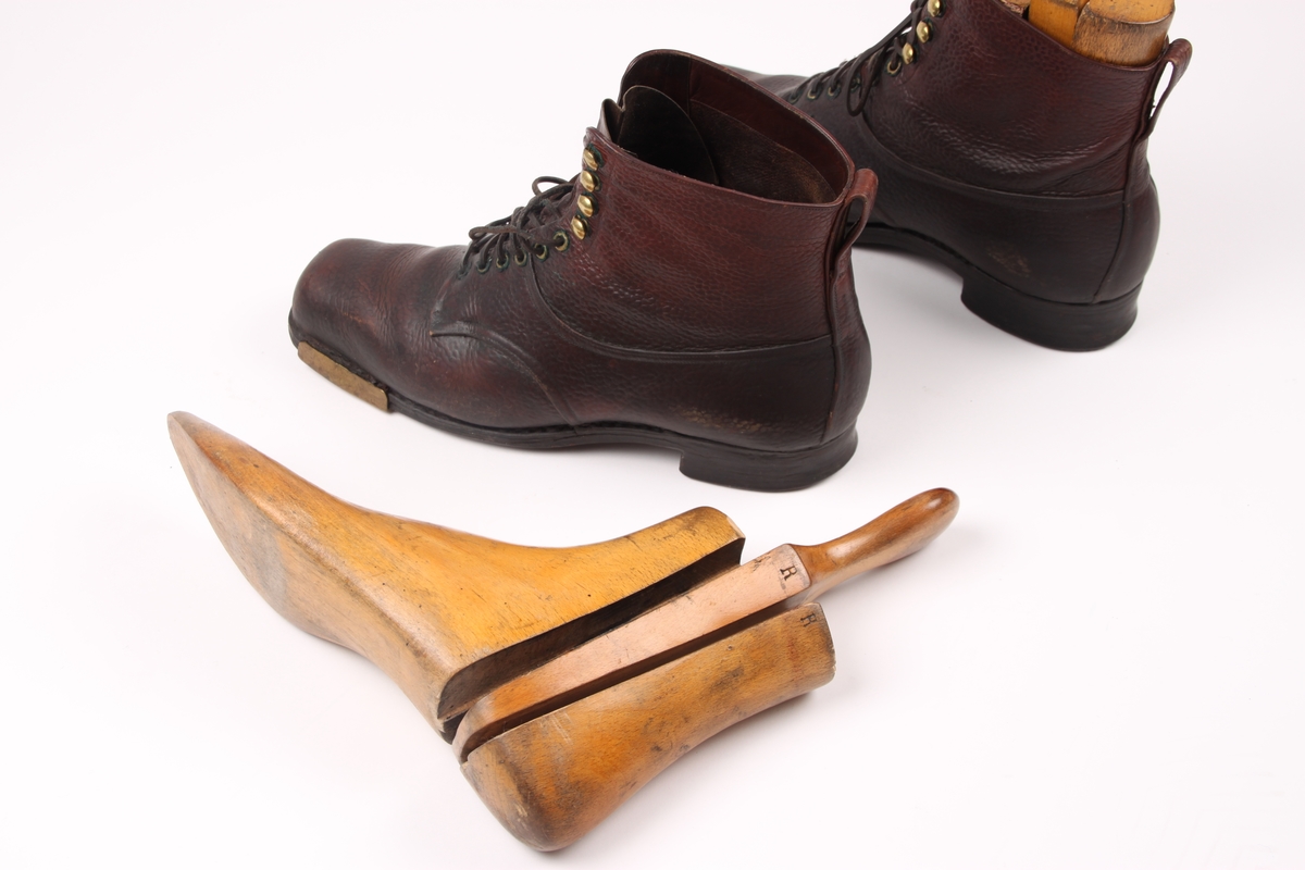 Et par beksømstøvler i lær med maljer i metall samt messingbeslag på sålen. Støvlene har lærlisser med sølvbeslag og en hempe av skinn bak på hver sko. Trelester inne i skoene.