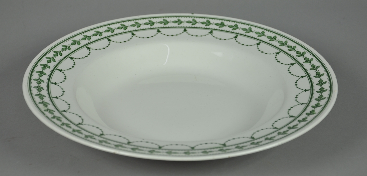 Rund og dyp suppetallerken av keramikk, steingods, med grønn bord. Borden består av eikekrans og guirlandere. Mønsteret heter Fontainebleau.
