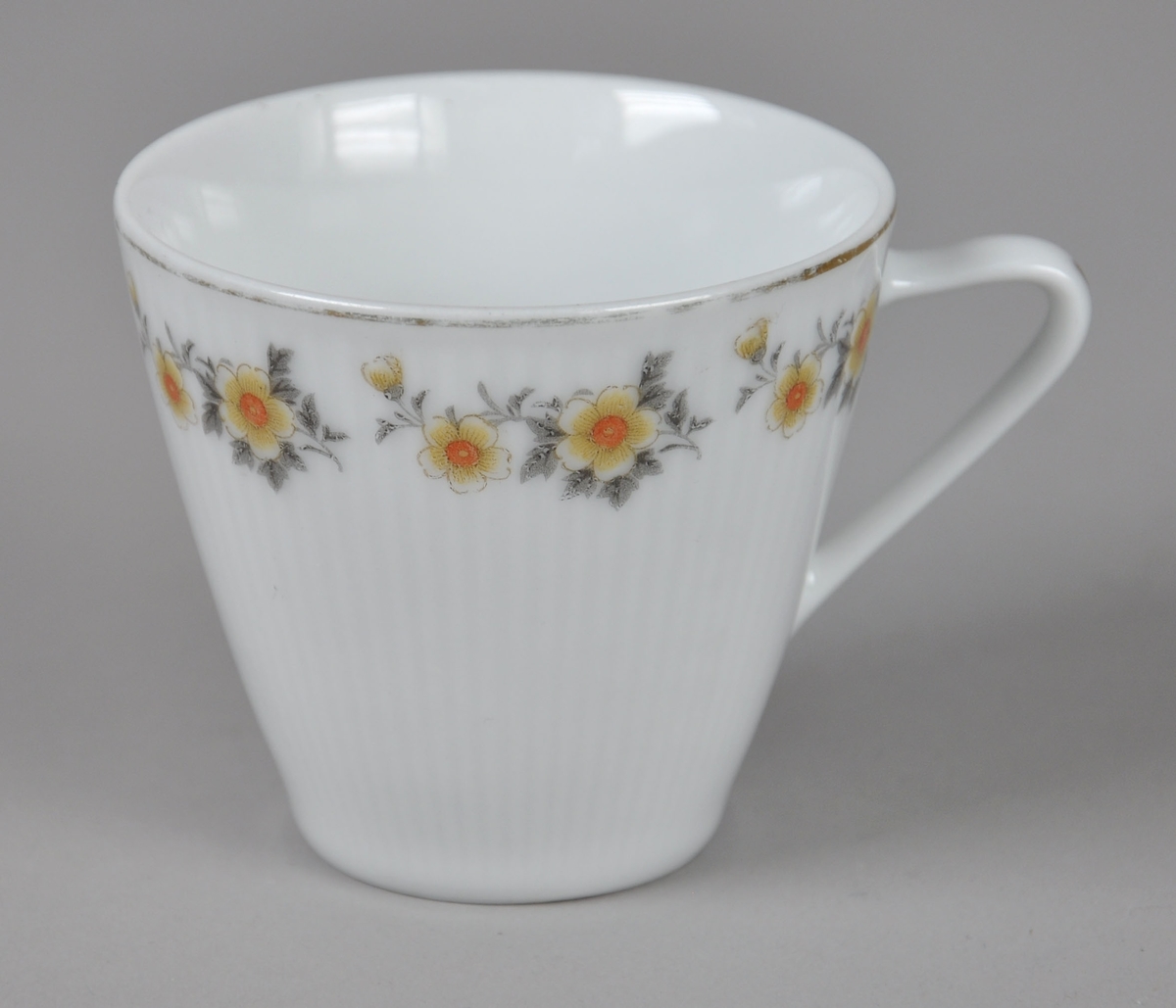 Kaffekopp av glassert keramikk, med hank. Koppen har malt dekor på utsiden med motiv av blomster og blader. Rundt munningsrand og på hanken er det påmalte sølvstriper.
