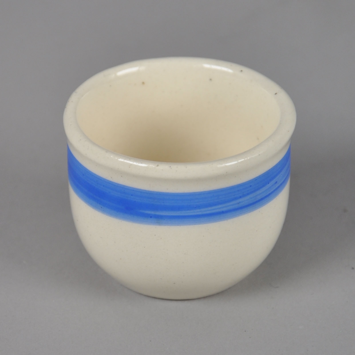 Eggeglass av glassert keramikk, med påmalt blå stripe ved kanten.