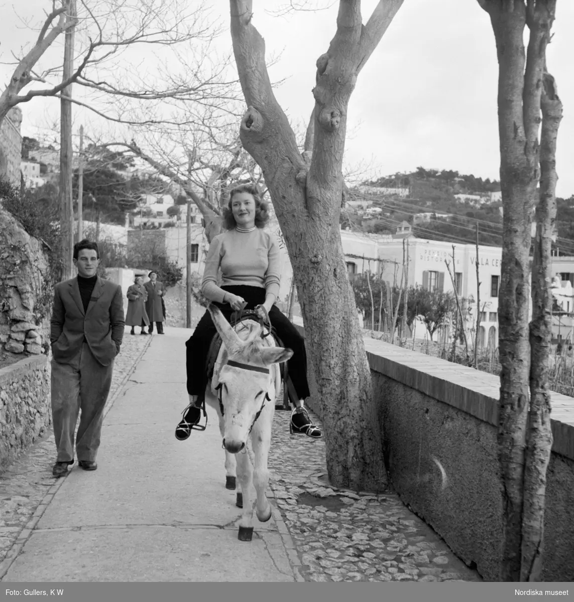 En flicka som rider på en åsna och en man går bredvid med händerna i byxfickorna