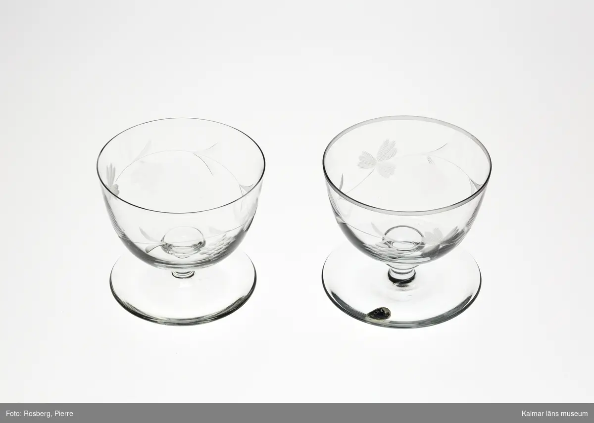 KLM 45817:1-2 Glas, dricksglas på fot. Med slipad dekor, i form av blad och druvklasar. Försedd med etikett, oval, blå botten text i silver: Kalmar och två stjärnor.