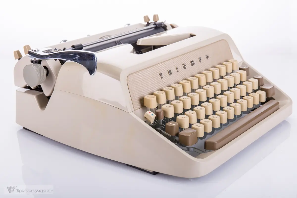 Liten mekanisk skrivemaskin med stålskjelett og plast- karosseri. Bæreveske i skai og papp.