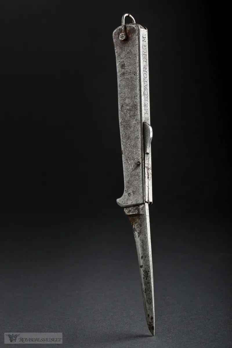 Foldbar tyskprodusert lommekniv. Kniven har to rom, et for hovedknivbladet, og et for en syl og en boksåpner. En liten hempe i metall er naglet fast i bakkant av kniven.