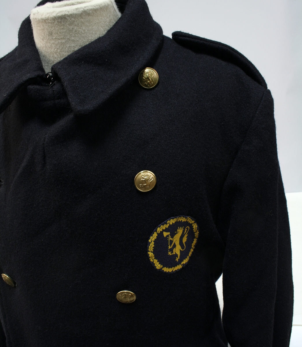 Dobbeltkneppet frakk med politimerke sydd på brystet.