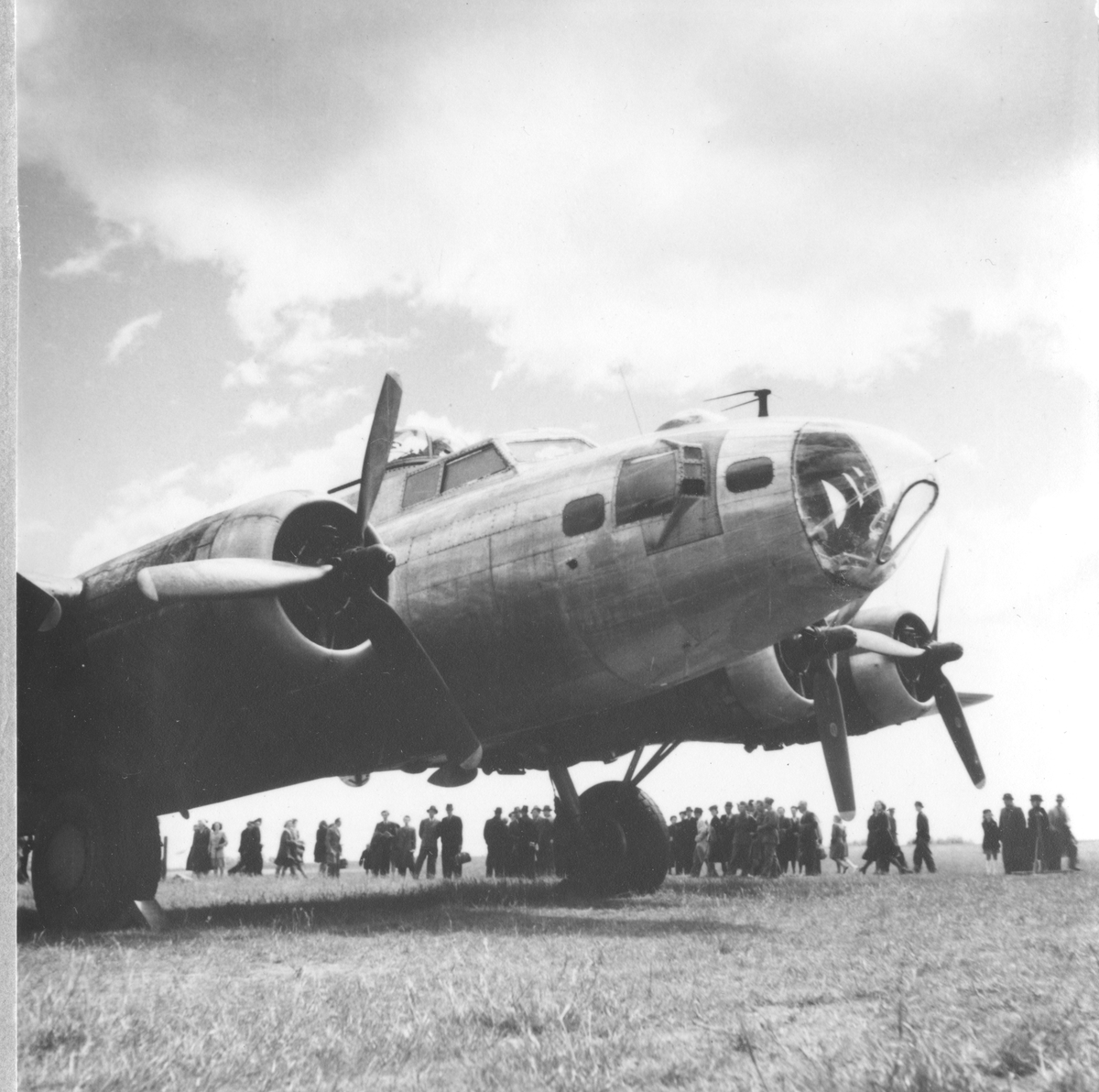 Närbild. Amerikanska bombflygplanet Boeing B-17 Flying Fortress står på ett flygfält. I bakgrunden står en folksamling.