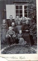 Familiegruppe. Syv barn og to voksne foran en husvegg. Kledd