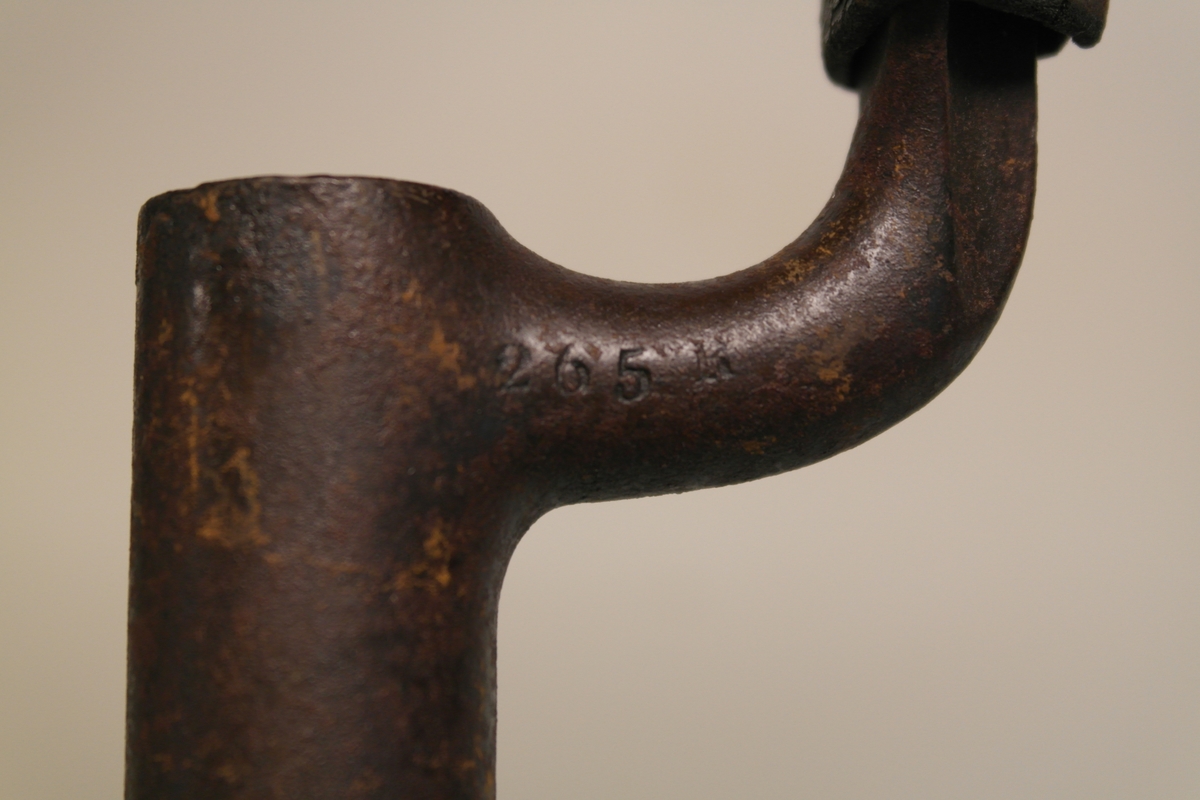 Stålbajonett med slire. Bajonetten er støpt. Sort lærslire med messingdupp og hempe. Sliret er sydd,  påmontert støpt messingfeste.