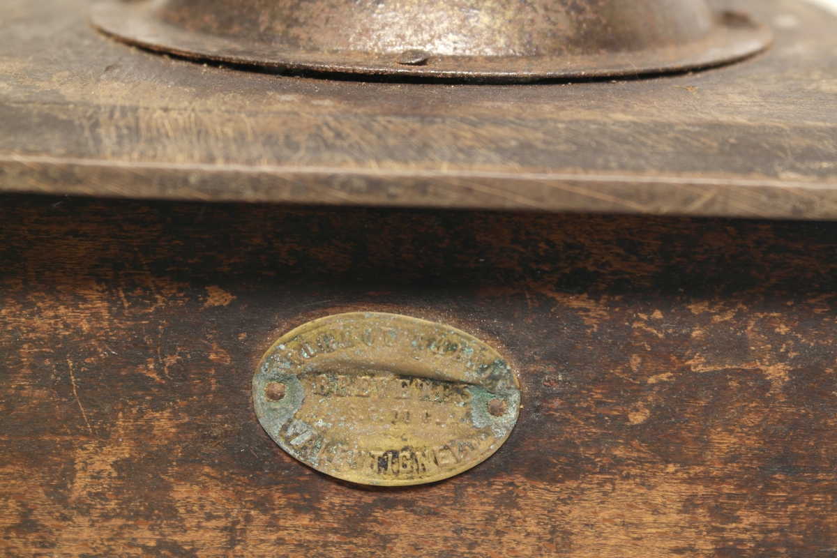 Kaffekvern (a og b) i tre, jern og messing. 
a) Kvadratisk kasse med topplate og bunnplate. Sveiv som går ned til innsatt tannhjul, som kverner kaffebønnene. Klokkeformet deksel som kan åpnes med en klaff som skyves til siden. Messingskilt med stempel.
b) Skuff som samler opp den malte kaffen. Stiftet i hjørner og bunnplate.