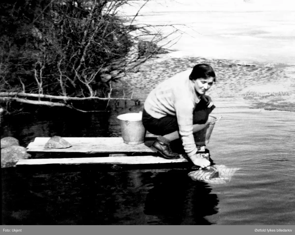 Skylling av klesvask i Rømsjøen i Rømskog. Kvinnen er G. Bergli, ca. 1938.