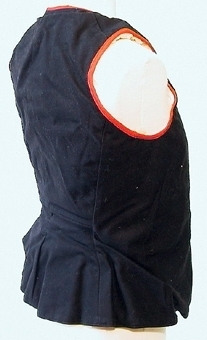 Livstycke för kvinna av svart kläde, kantat med röda ylleband. Livstycket är fodrad med getskinn och knäpps med nio st små mörkgrå knappar.
