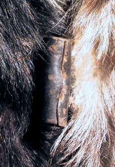 Hundskinnspäls i grått och svart. Ärmarna är fodrade med ett grått bomullstyg och övriga pälsen är fodrad med ett svart, kypertvävt ylletyg. Pälsen har två stora fickor med lock och tygklädda knappar på insida. Fyra knappar gjorda av hårt hoprullat, barkgarvat skinn. Hyskor på motsvarande sida av skinnremsor. Kragen går att fälla upp och för att hålla den på plats löper en skinnsnodd i sex metallringar på kragens baksidan. Snodden går att knyta ihop under hakan. Mitt bak är det ett sprund. På insidan kragen sitter en hank av flätade skinnremsor.